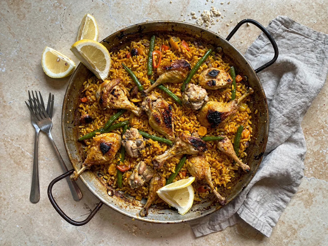Paella valenciana en su paellera vista desde arriba, con cubiertos y trapo